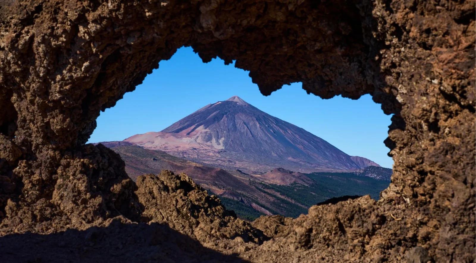 Mount Teide framed through a natural opening in a weathered lava rock formation