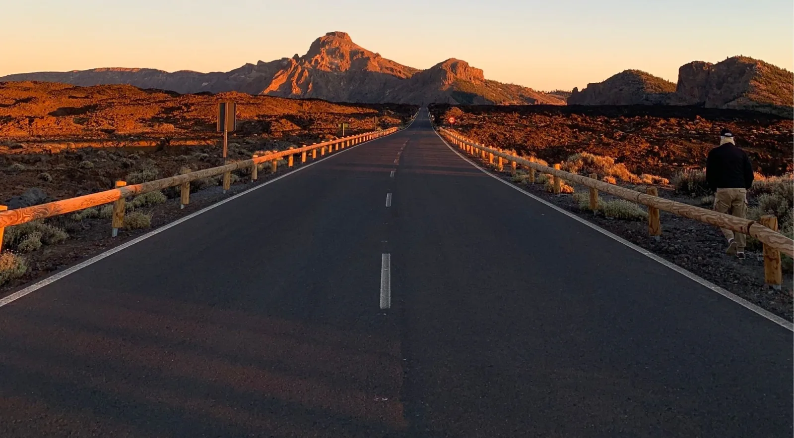 The mountain road running straight through a black lava field at sunset, wooden barriers glowing orange