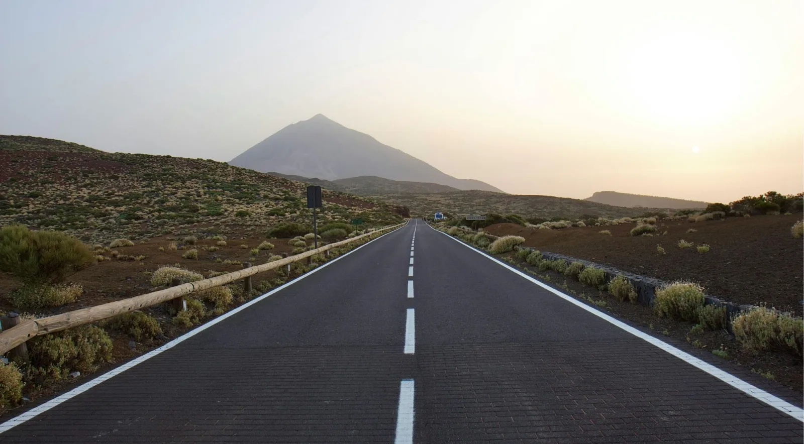 A straight stretch of the Teide park road at dusk with the volcano silhouetted ahead