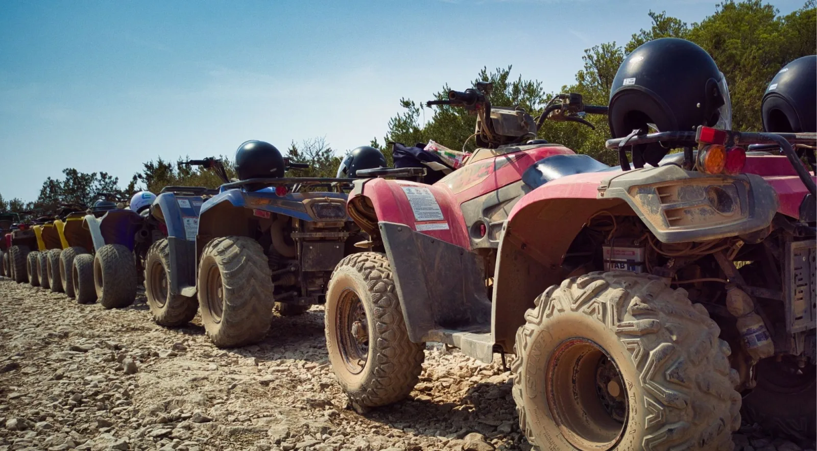 A line of quad bikes parked on gravel with helmets resting on the handlebars before a tour